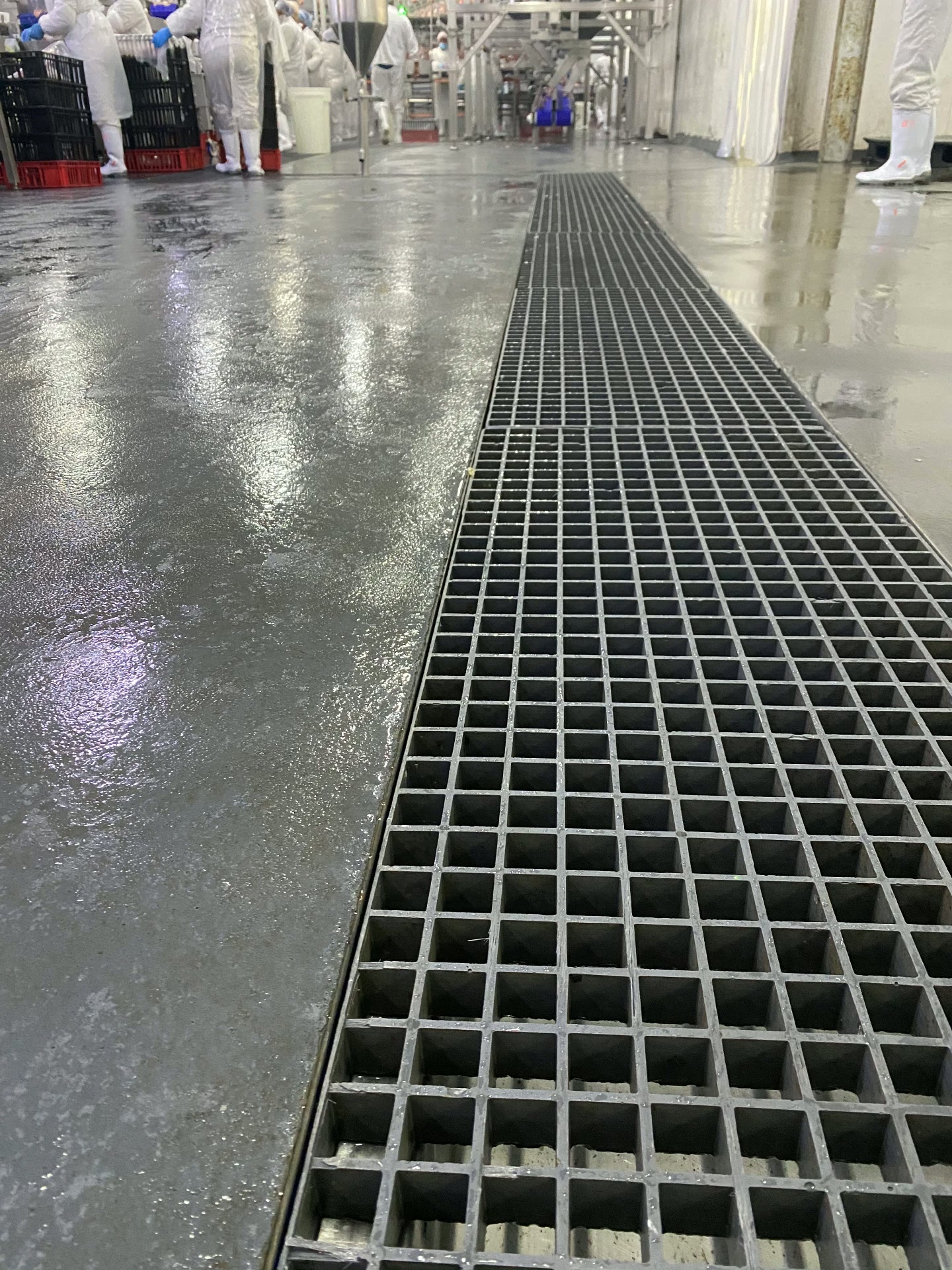 Stainless steel drainage channel with grey grating running the length of a wet processing floor in a food facility