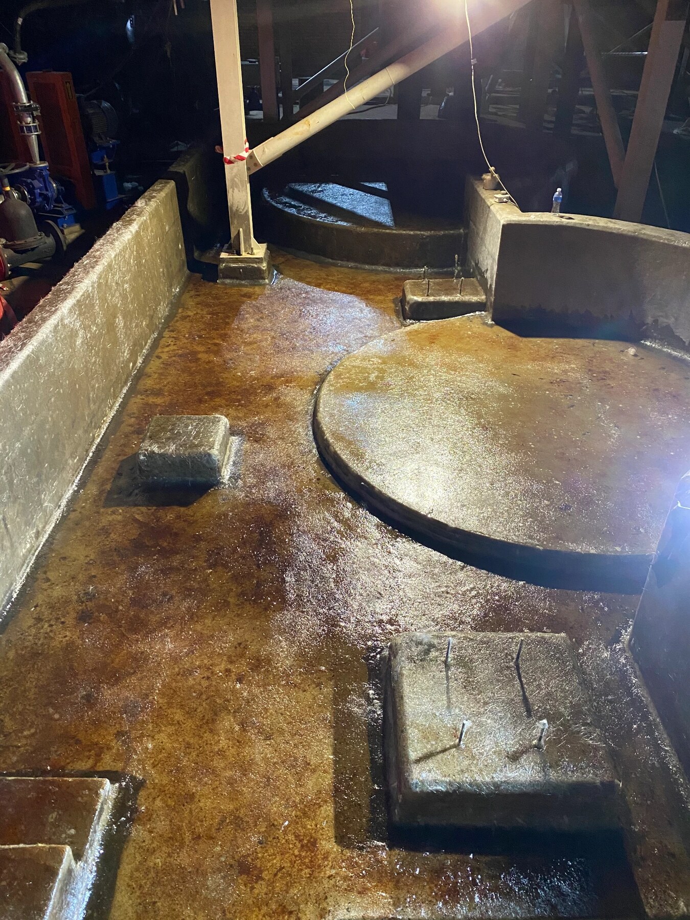 Glossy amber chemical-resistant lining covering a concrete bund floor with raised equipment plinths and protruding anchor bolts, with pumps and pipework behind